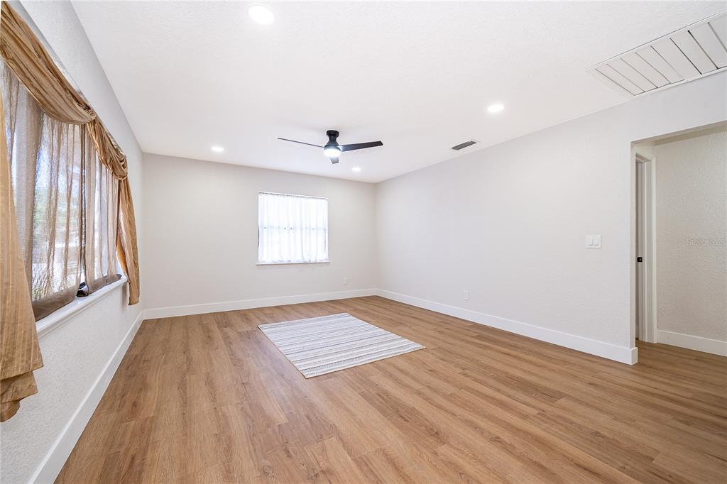 A bright, empty room features light wood-look flooring, white walls, a ceiling fan, and windows — 1914 BONANZA COURT, WINTER PARK, FL