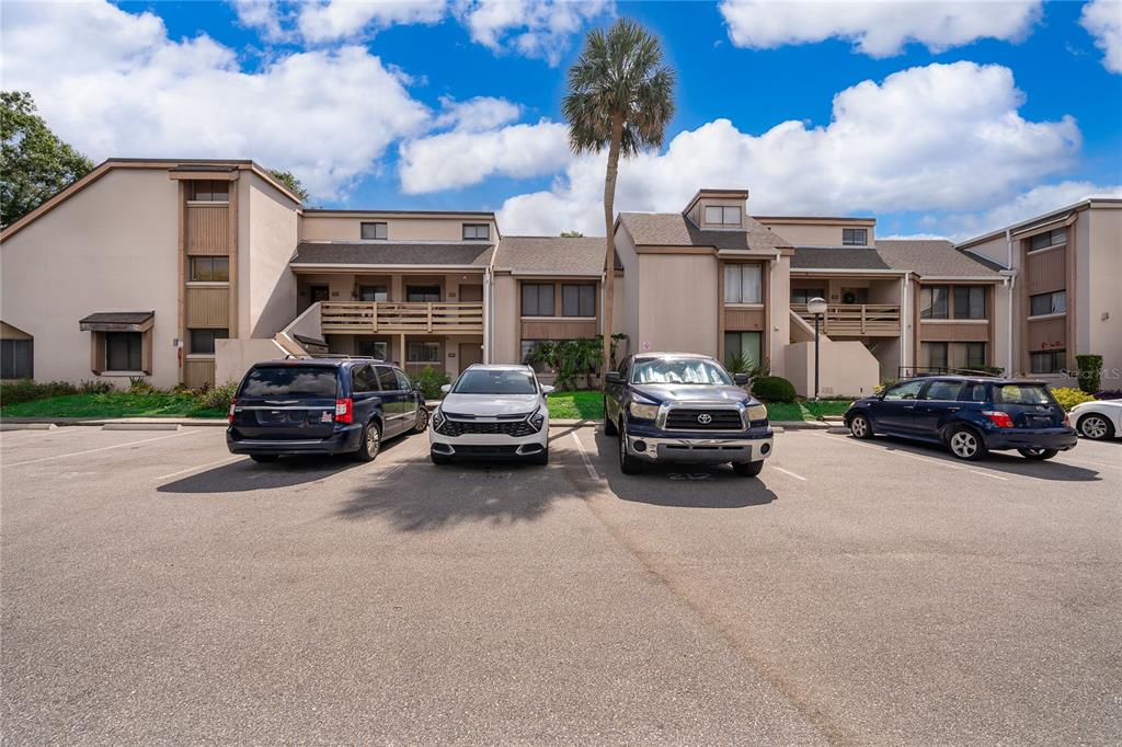 A multi-story apartment complex features beige siding, balconies, and a parking lot with several cars — 228 ORIENTA POINT STREET UNIT 228, ALTAMONTE SPRINGS, FL