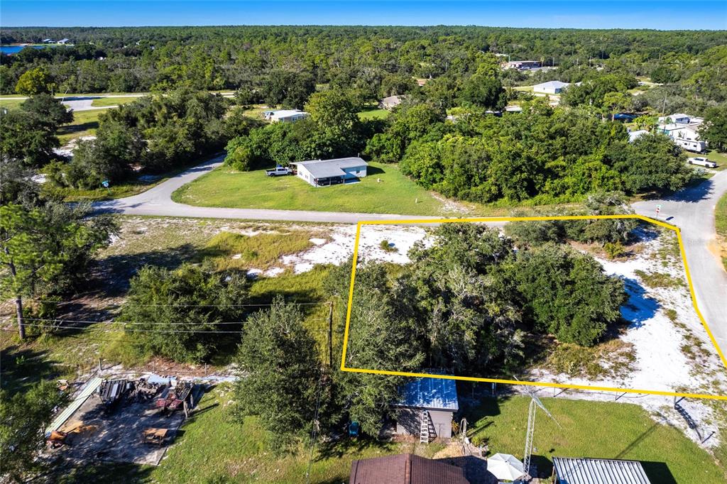 An aerial view shows a vacant, tree-covered lot outlined in yellow near a paved road — 3048 OLEANDER DRIVE, LAKE PLACID, FL
