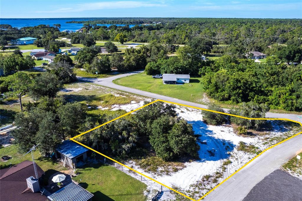 An aerial view shows a vacant, sandy residential lot outlined in yellow near a road — 3048 OLEANDER DRIVE, LAKE PLACID, FL