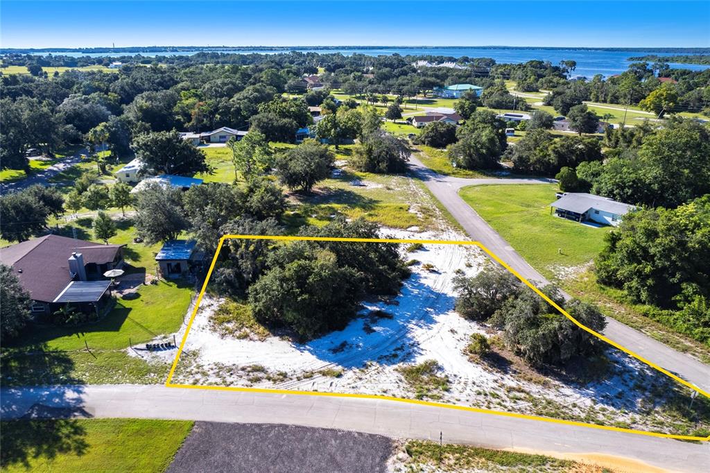 An aerial view shows a vacant, sandy residential lot outlined in yellow near a road — 3048 OLEANDER DRIVE, LAKE PLACID, FL