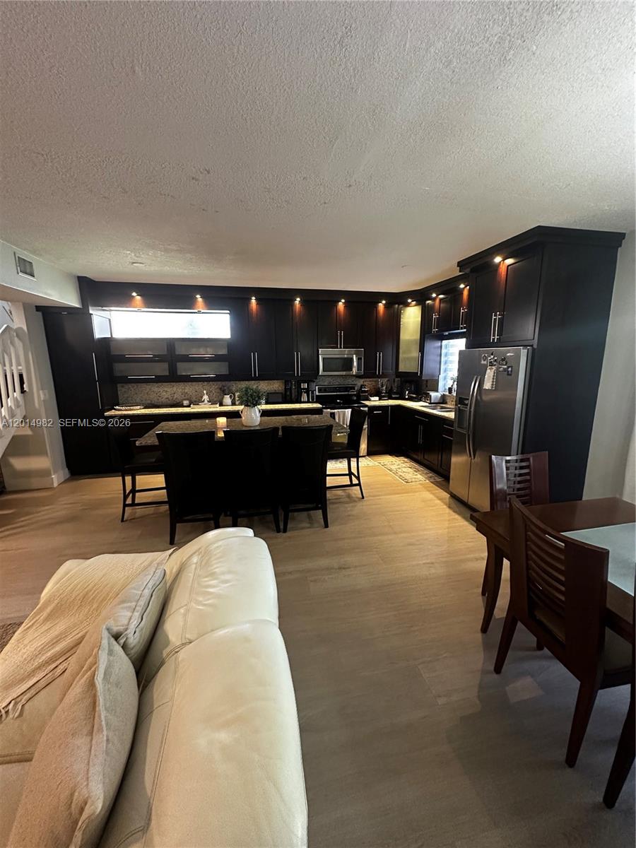 A kitchen features dark wood cabinetry, stainless steel appliances, and a central island with seating — 8211 NW 191st Ln # 35L, Hialeah FL 33015, HIALEAH, FL
