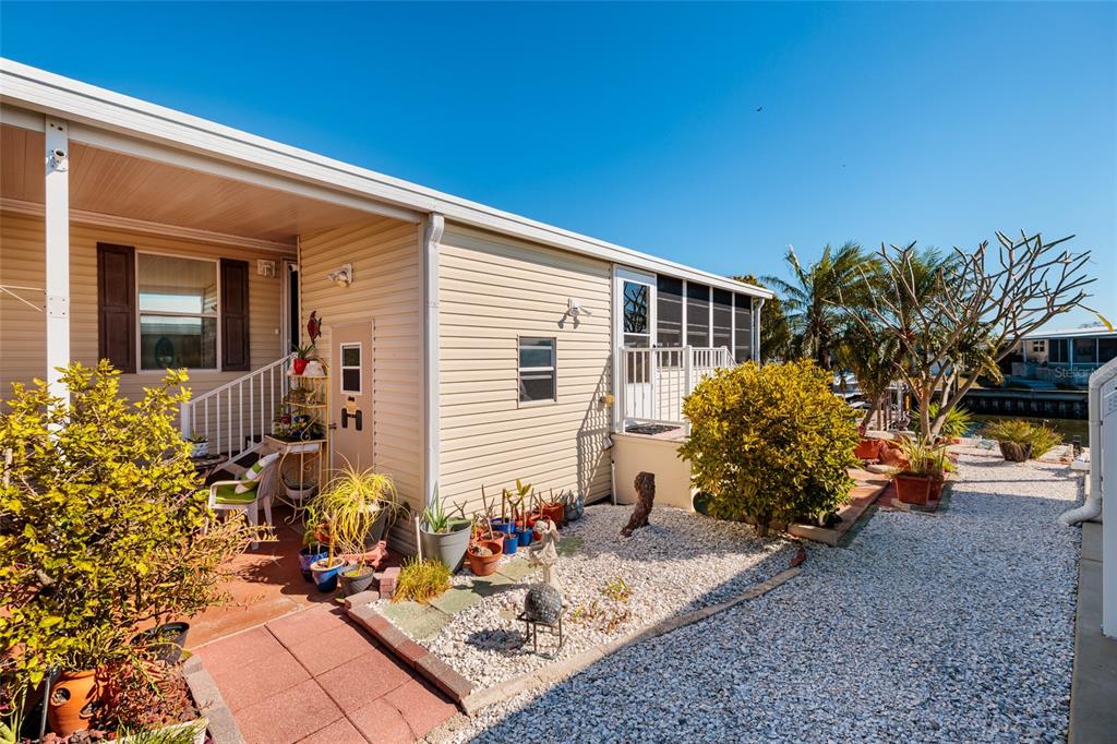 The exterior of a beige mobile home features a covered patio, gravel landscaping, and potted plants — 134 AMERICANA COURT NE UNIT 216, ST PETERSBURG, FL