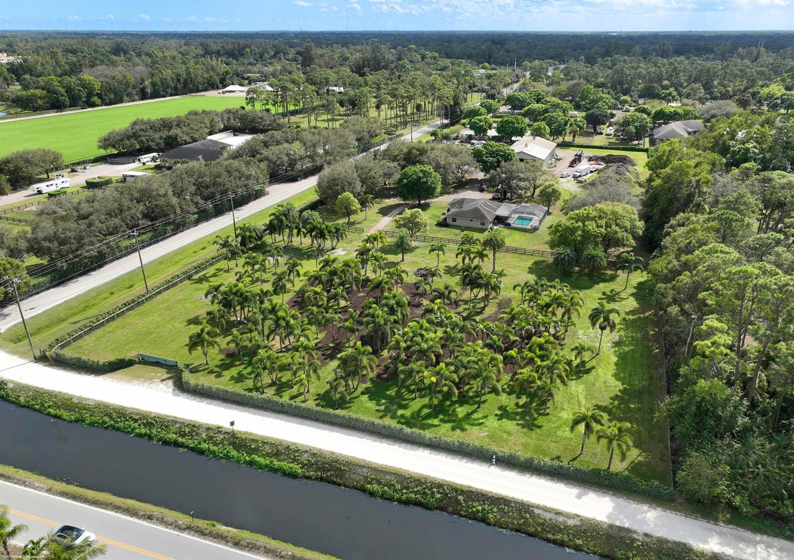 An aerial view shows a house with a pool surrounded by palm trees and greenery — 13528 N 6th Court N, FL 33470, FL