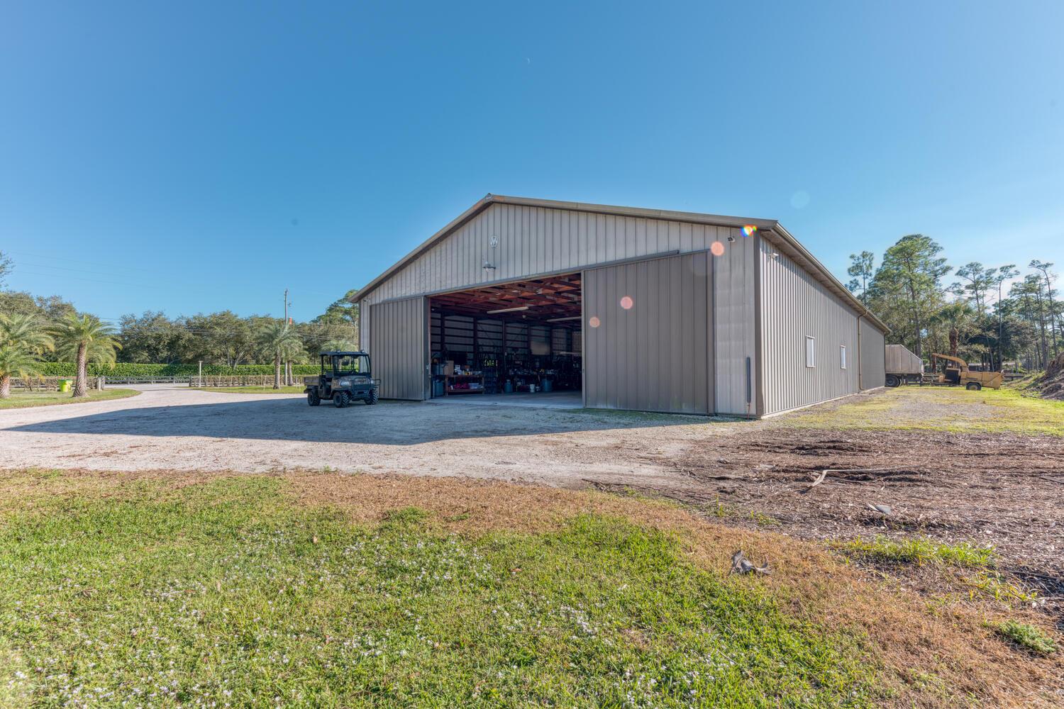 A large metal-sided barn with a wide open sliding door sits on a gravel lot — 13528 N 6th Court N, FL 33470, FL