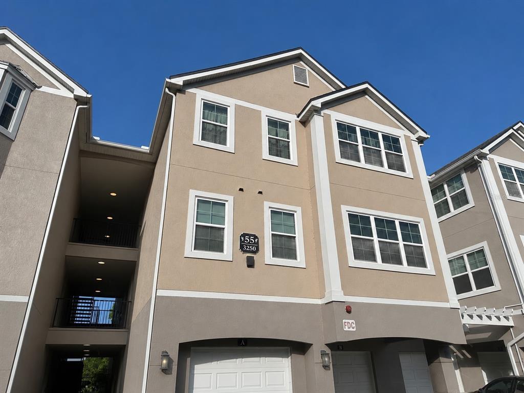 The exterior of a multi-story tan apartment building features white-trimmed windows and garage doors — 3250 CORONA VILLAGE WAY UNIT 206, ORLANDO, FL