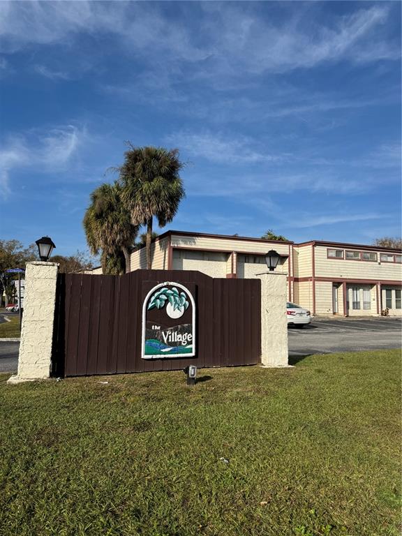 A brown wooden sign for The Village stands in front of a multi-unit residential building — 3990 CRAYRICH CIRCLE UNIT GE, ORLANDO, FL