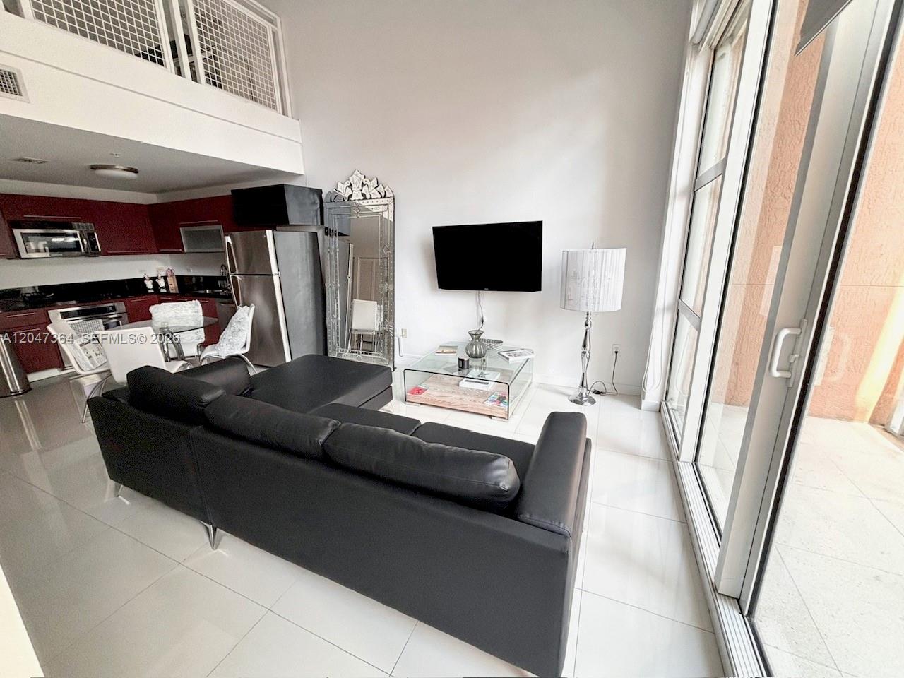 A living room with a black sectional sofa, glass coffee table, and adjacent kitchen area — 244 Biscayne Blvd # 451, Miami FL 33132, MIAMI, FL