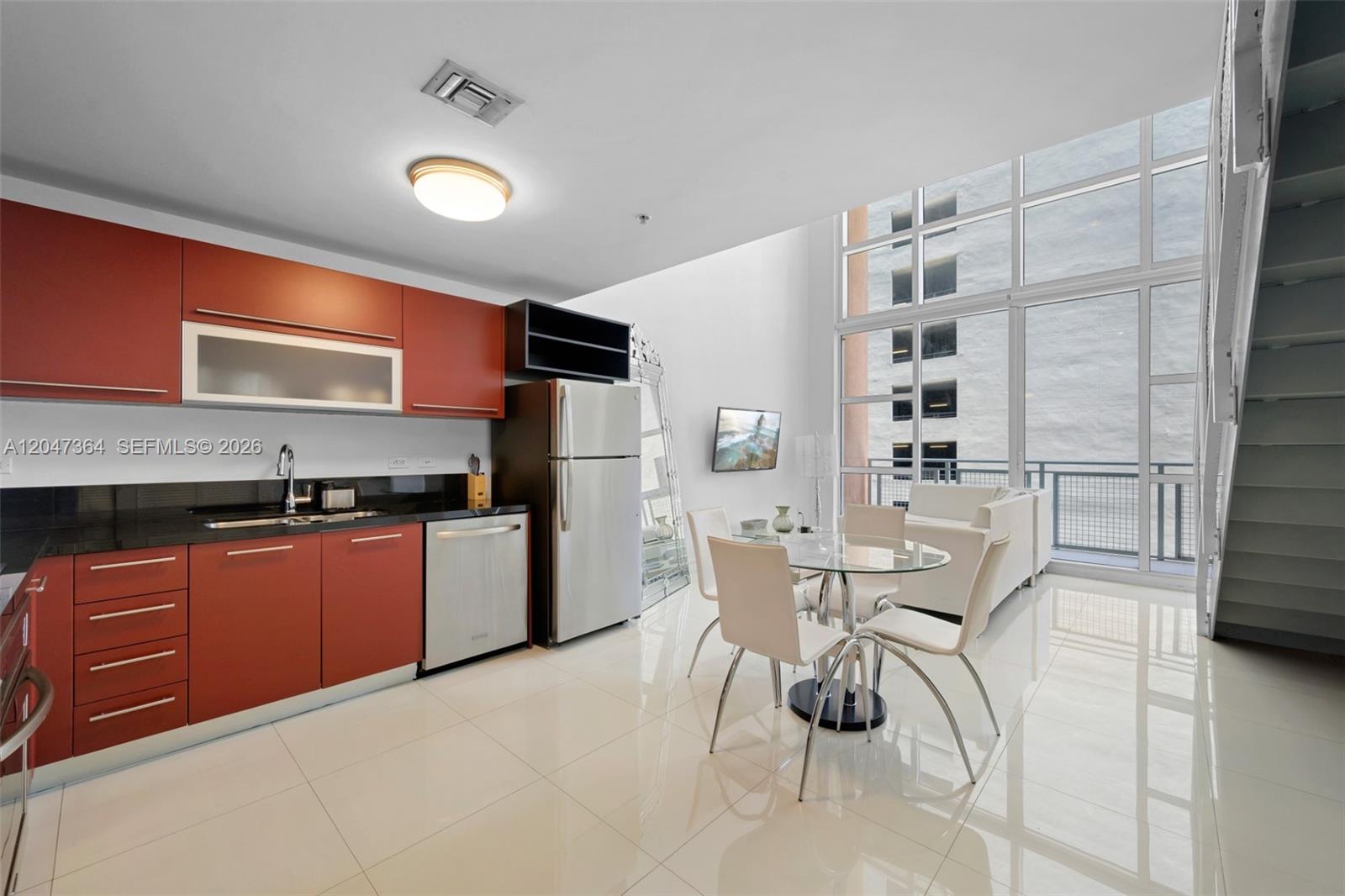 A modern kitchen and dining area feature red cabinets, stainless appliances, and floor-to-ceiling windows — 244 Biscayne Blvd # 451, Miami FL 33132, MIAMI, FL