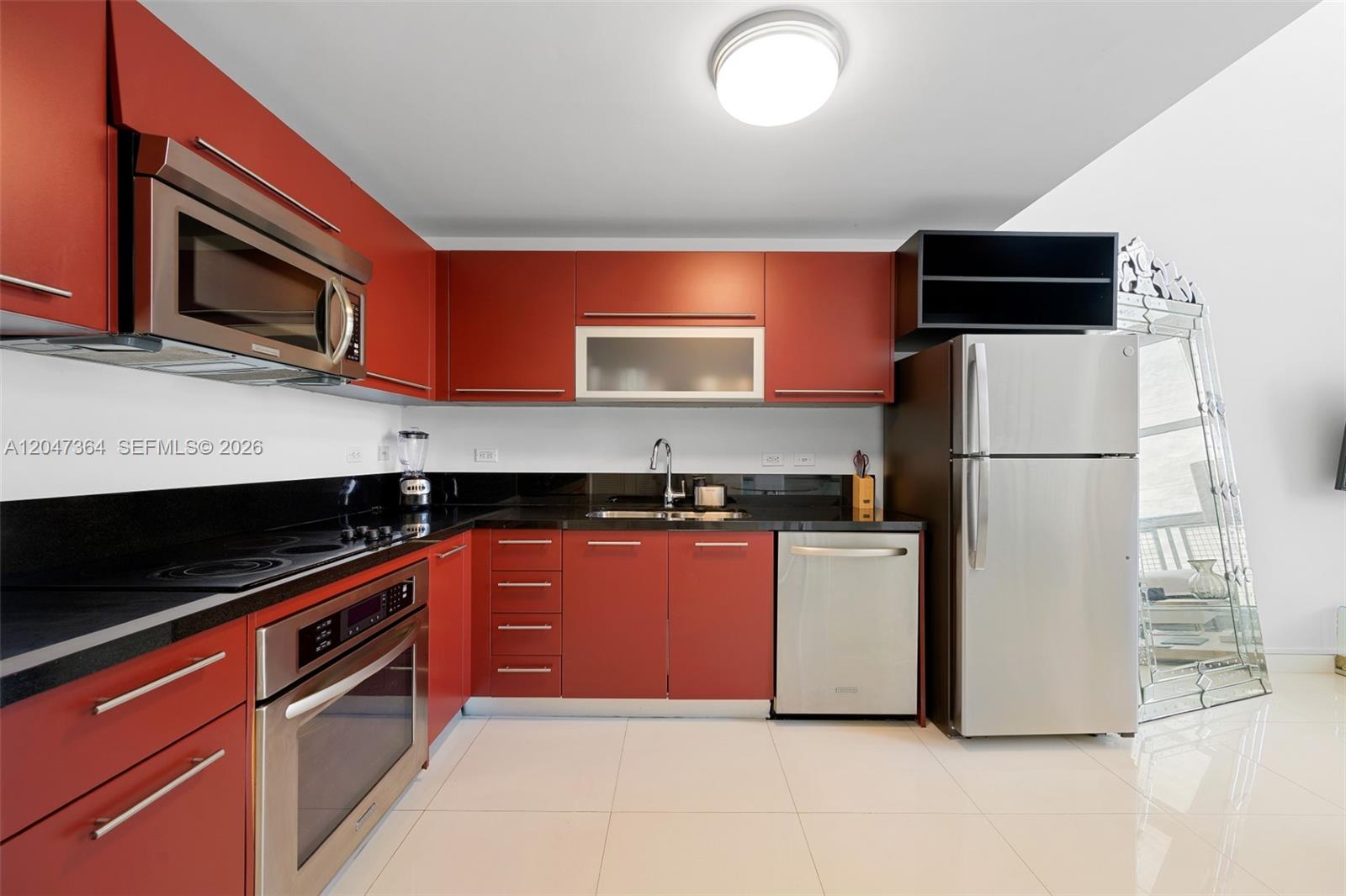 A kitchen features red cabinets, black countertops, stainless steel appliances, and white tile flooring — 244 Biscayne Blvd # 451, Miami FL 33132, MIAMI, FL