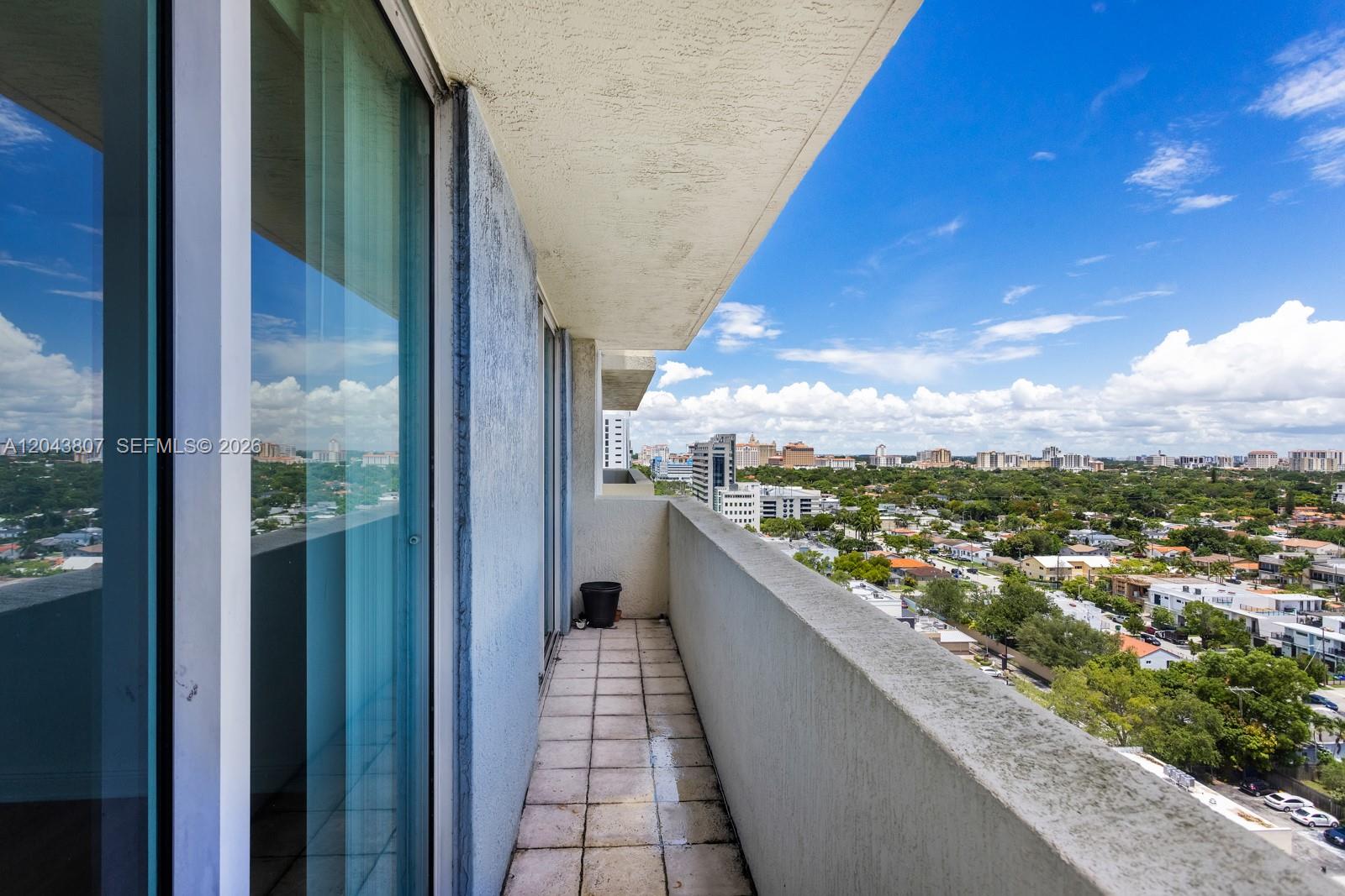 A high-rise balcony with tiled flooring overlooks a suburban cityscape under a blue sky — 3000 CORAL WAY # 1507, Miami FL 33145, MIAMI, FL