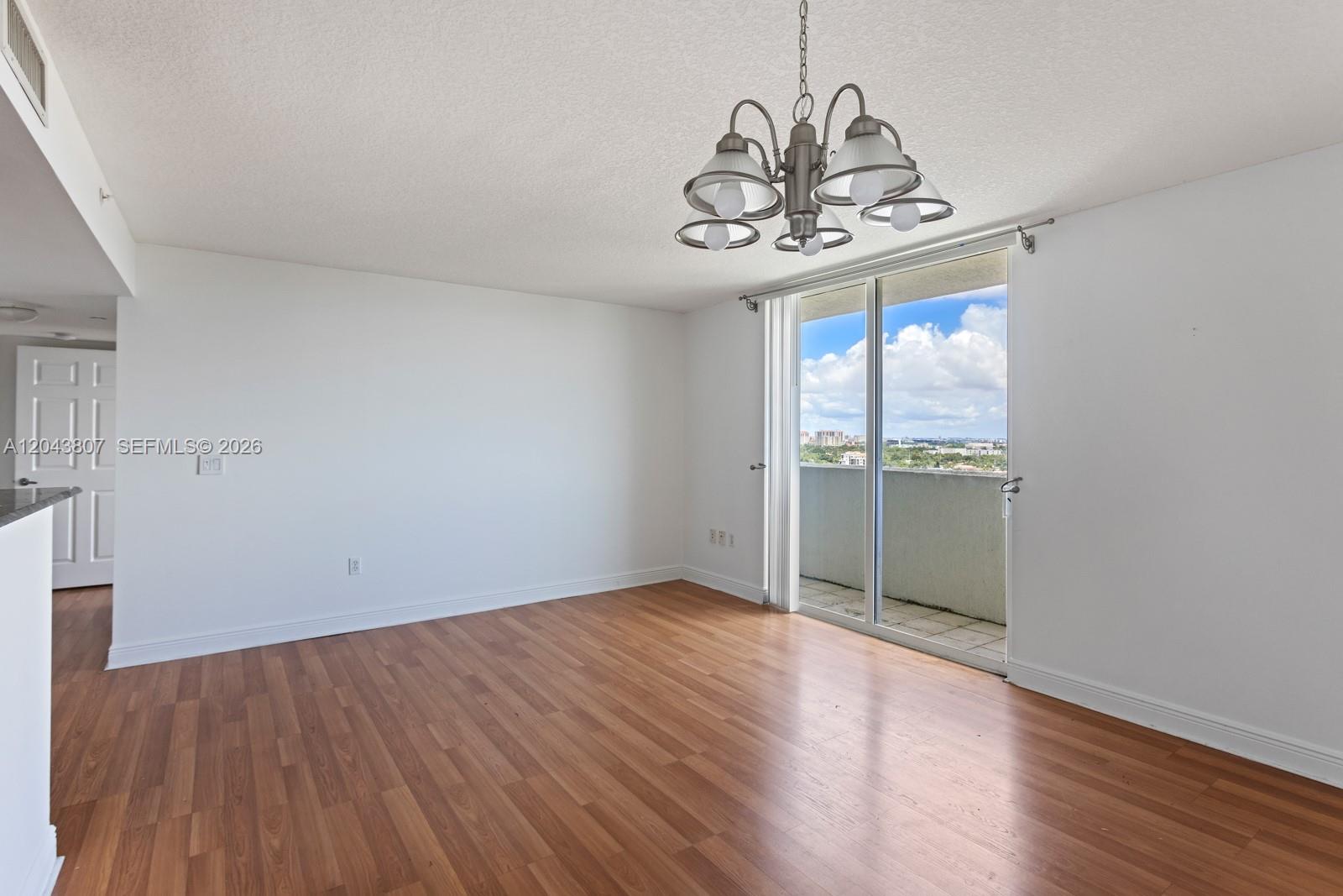 An empty room features wood-look flooring, a chandelier, and a sliding glass door to a balcony — 3000 CORAL WAY # 1507, Miami FL 33145, MIAMI, FL