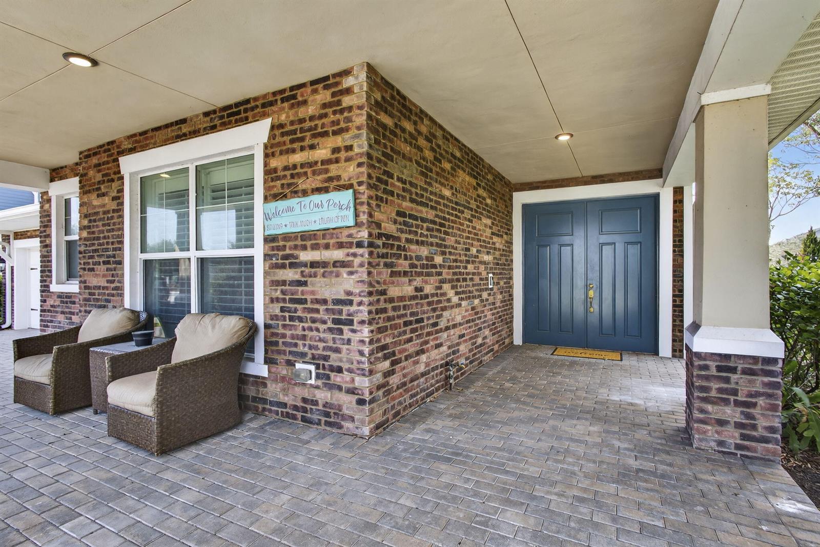 A brick-front porch features a blue double door, two wicker chairs, and a paved floor — 929 Sterling Pine Place, FL 33470, FL