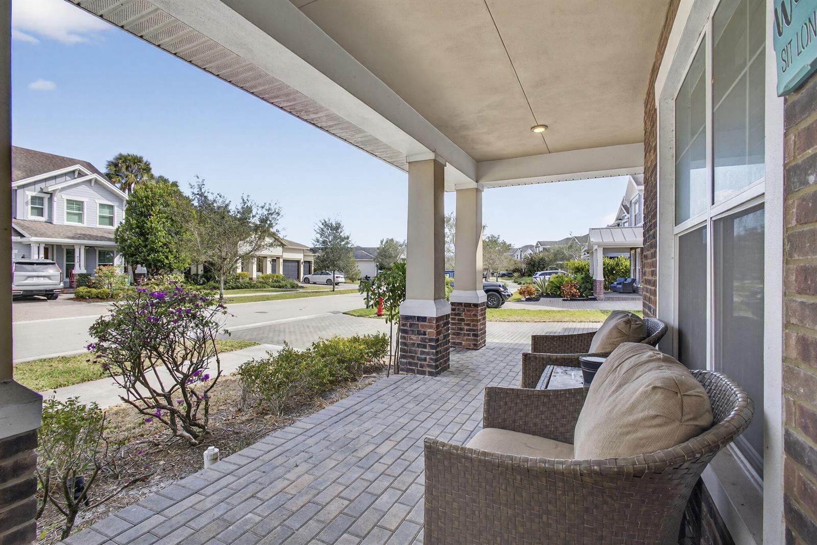 A covered brick porch features wicker chairs and views of a suburban residential street — 929 Sterling Pine Place, FL 33470, FL
