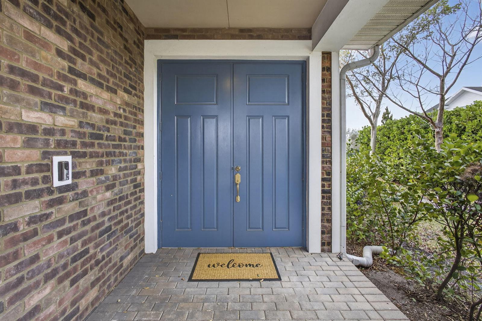 A blue double front door with a welcome mat sits on a brick porch — 929 Sterling Pine Place, FL 33470, FL