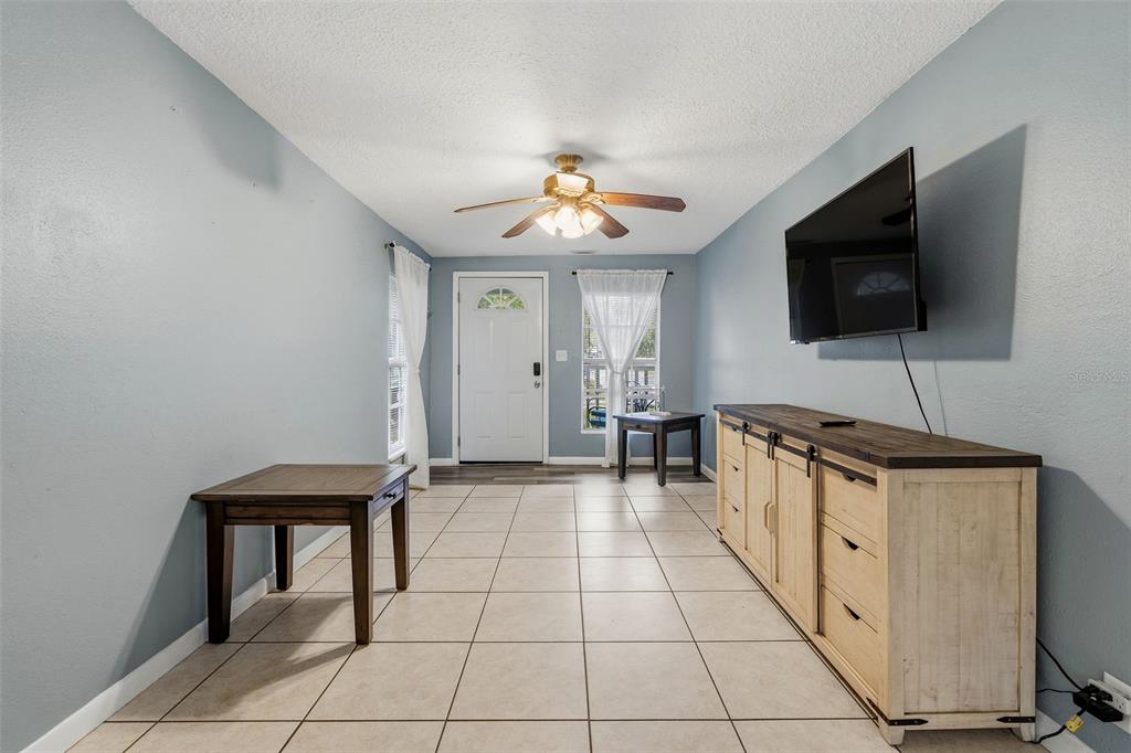 A living room features light blue walls, tile flooring, a ceiling fan, and a media console — 1171 HIGHLAND COURT N, ST PETERSBURG, FL