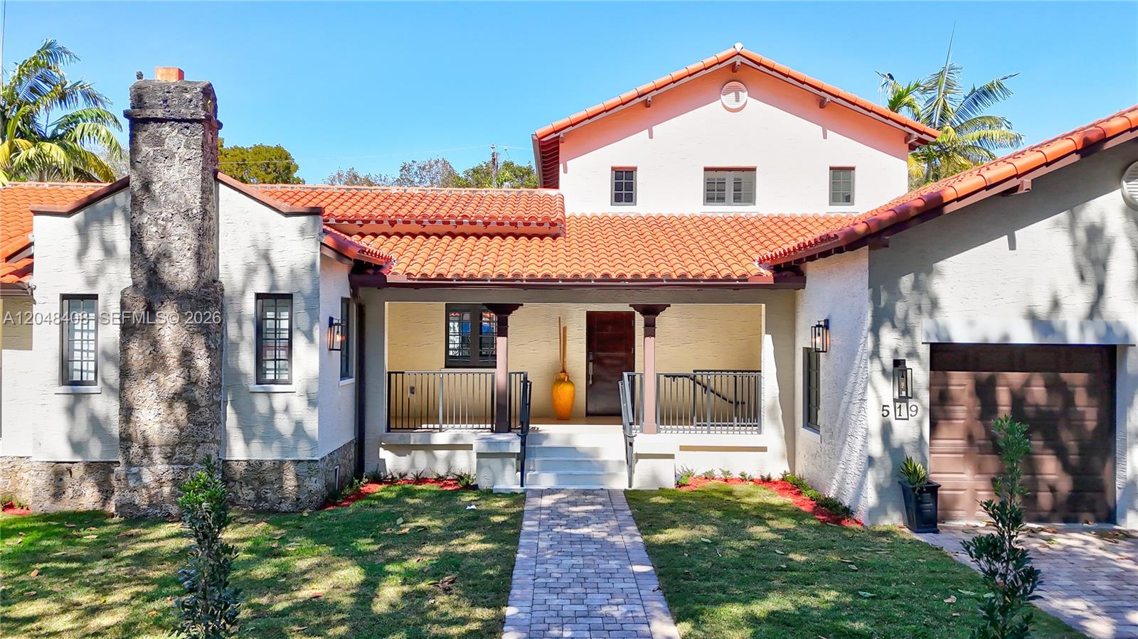 A Mediterranean-style house features a stone chimney, red tile roof, and a covered front porch — 519 Alhambra Cir, Coral Gables FL 33134, CORAL GABLES, FL