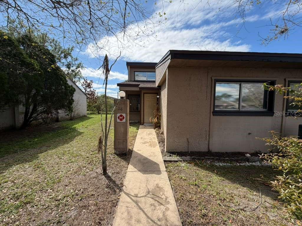 A concrete walkway leads to the front entrance of a tan, single-story residential building — 118 DAHLIA VILLAGE CIRCLE UNIT 79, ORLANDO, FL