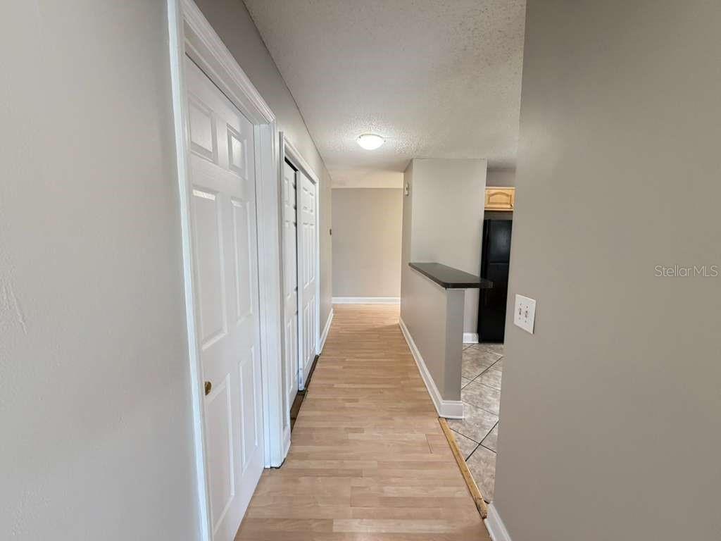 A hallway with light wood-look flooring leads toward a kitchen with a breakfast bar — 118 DAHLIA VILLAGE CIRCLE UNIT 79, ORLANDO, FL