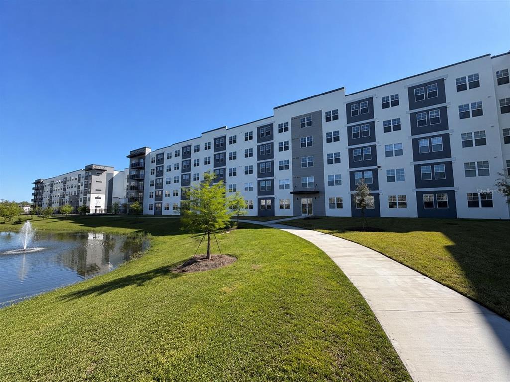 A multi-story apartment building stands next to a pond with a fountain and a sidewalk — 5587 MILLENIA PARK BOULEVARD UNIT 503, ORLANDO, FL