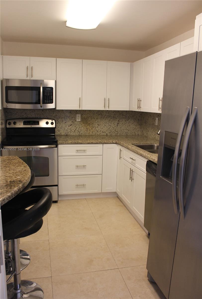 A kitchen features white cabinets, granite countertops, stainless steel appliances, and light tile flooring — 2333 Brickell Ave # 1004, Miami FL 33129, MIAMI, FL