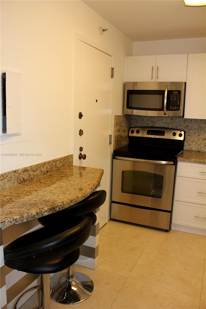 A kitchen features a granite breakfast bar, stainless steel appliances, and white cabinetry — 2333 Brickell Ave # 1004, Miami FL 33129, MIAMI, FL