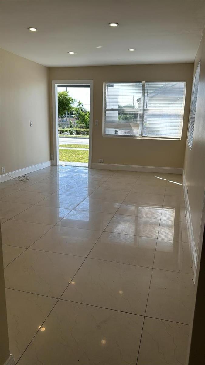 An empty room with beige walls, large light-colored floor tiles, and a glass-paned exterior door — 3734 Avenue S, Riviera Beach FL 33404, RIVIERA BEACH, FL