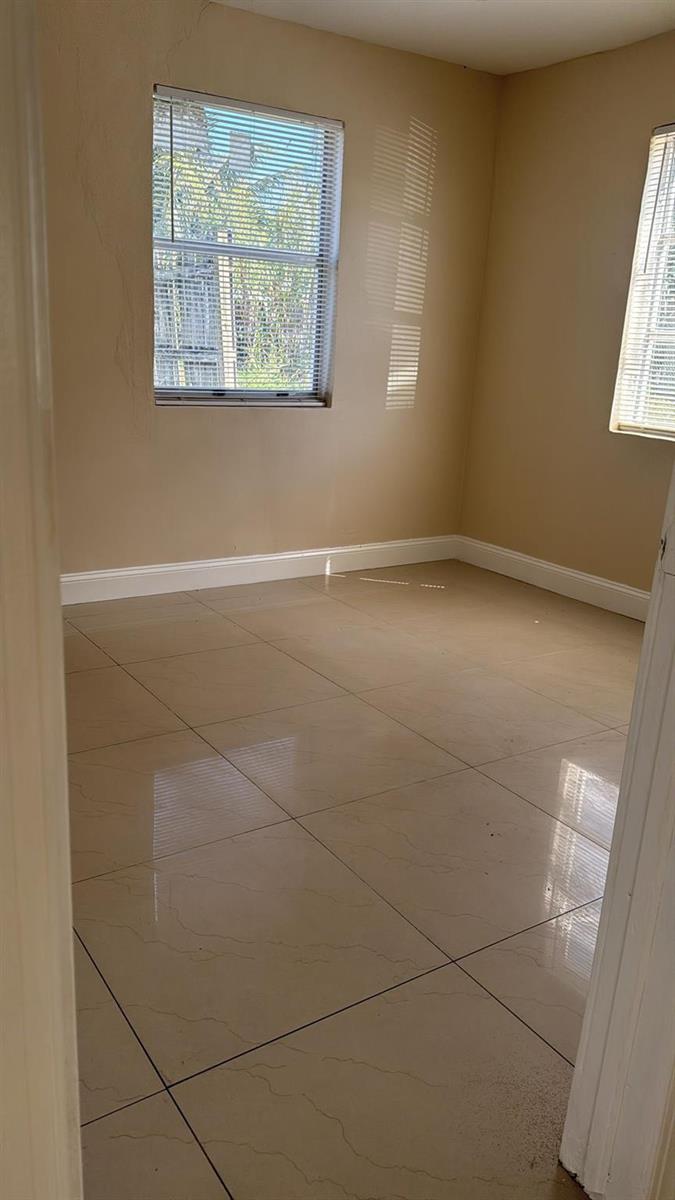An empty room with beige walls, large light-colored floor tiles, and two windows with blinds — 3734 Avenue S, Riviera Beach FL 33404, RIVIERA BEACH, FL