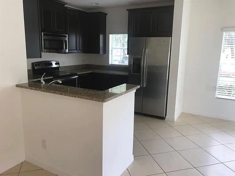 A kitchen features dark wood cabinets, granite countertops, stainless steel appliances, and light tile flooring — 2890 TANZANITE TERRACE, KISSIMMEE, FL