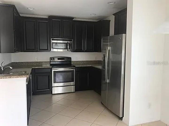 A kitchen features dark wood cabinets, stainless steel appliances, and light-colored tile flooring — 2890 TANZANITE TERRACE, KISSIMMEE, FL