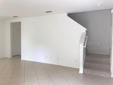 A room with tiled floors, a white wall, and carpeted stairs leading to an upper level — 2890 TANZANITE TERRACE, KISSIMMEE, FL