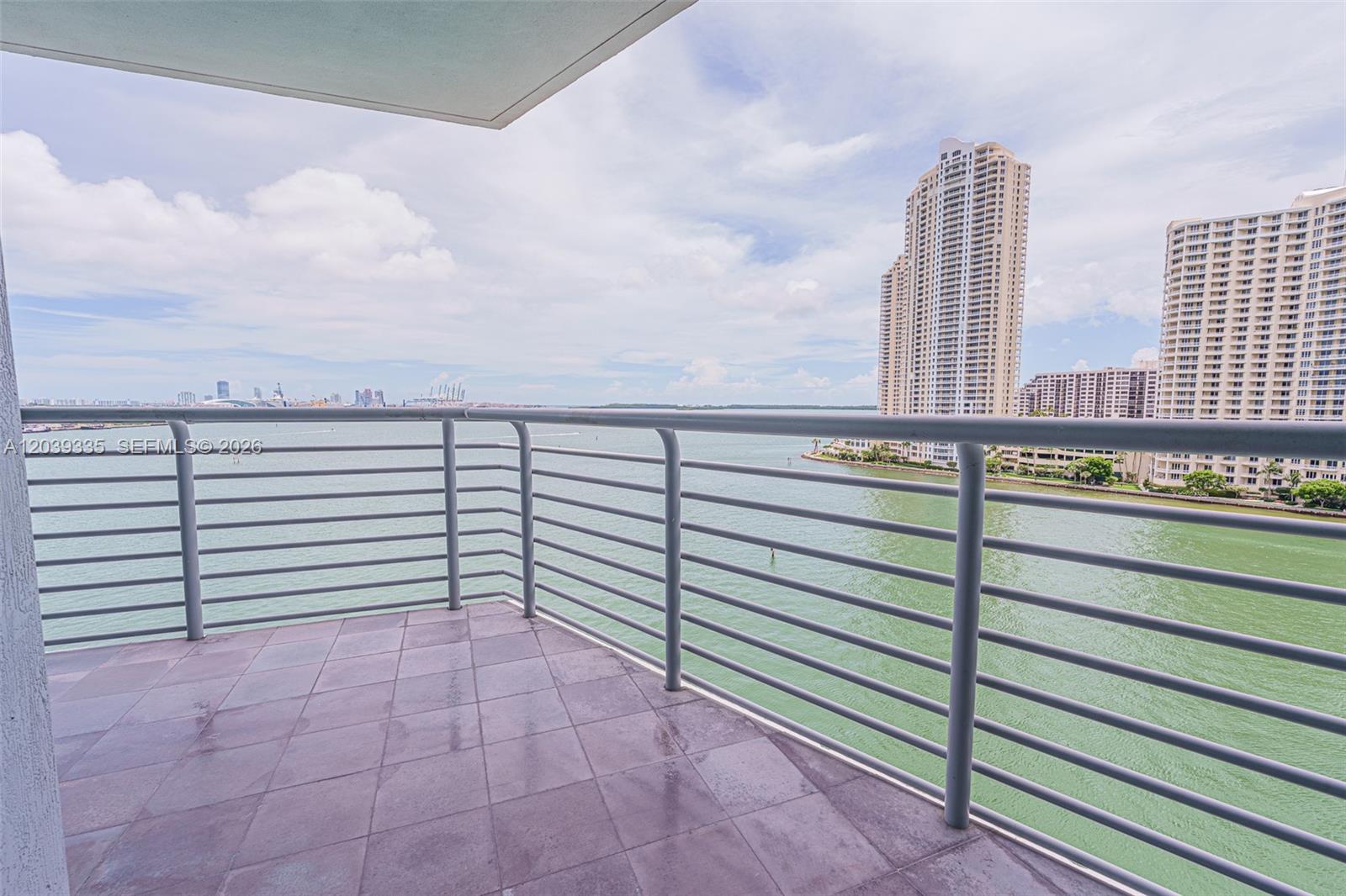 A balcony with tiled flooring and metal railings overlooks a bay and high-rise buildings — 335 S Biscayne Blvd # 1009, Miami FL 33131, MIAMI, FL