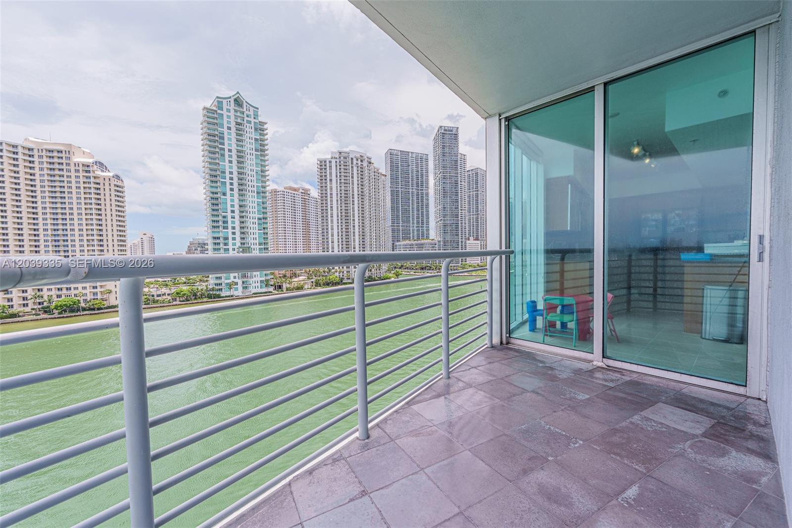 A balcony with gray tile flooring overlooks a body of water and city skyscrapers — 335 S Biscayne Blvd # 1009, Miami FL 33131, MIAMI, FL