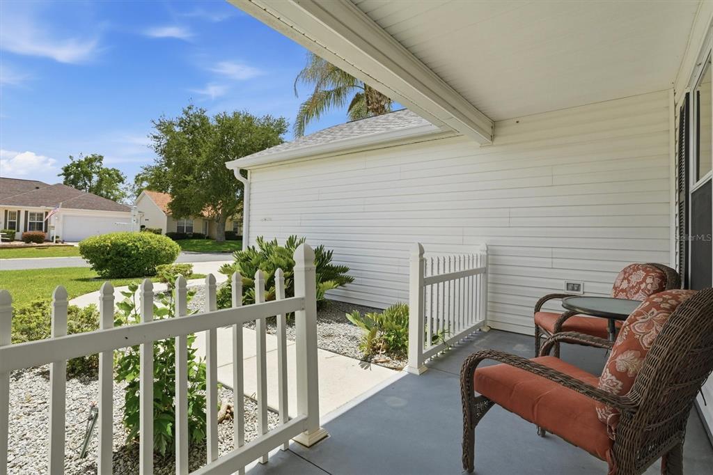 A covered porch with white railings, wicker chairs, and a view of a suburban street — 3425 CARBONDALE COURT, THE VILLAGES, FL