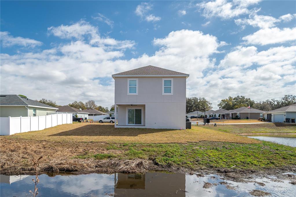 A two-story house with a light-colored exterior sits near a pond and a white fence — 2169 SUTTON RIDGE AVENUE, LAKELAND, FL