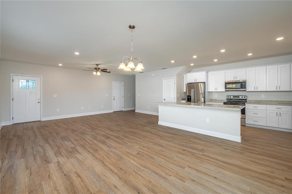 An open-concept kitchen and living area features light wood flooring, white cabinetry, and recessed lighting — 2169 SUTTON RIDGE AVENUE, LAKELAND, FL