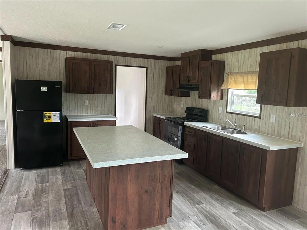 A kitchen features dark wood cabinets, a central island, black appliances, and light-colored countertops — 3548 VALLEY TRAIL, LAKELAND, FL