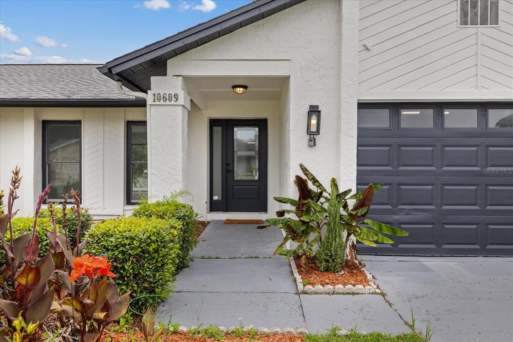 The exterior of a white house features a dark gray front door and garage door — 10609 OUT ISLAND DRIVE, TAMPA, FL