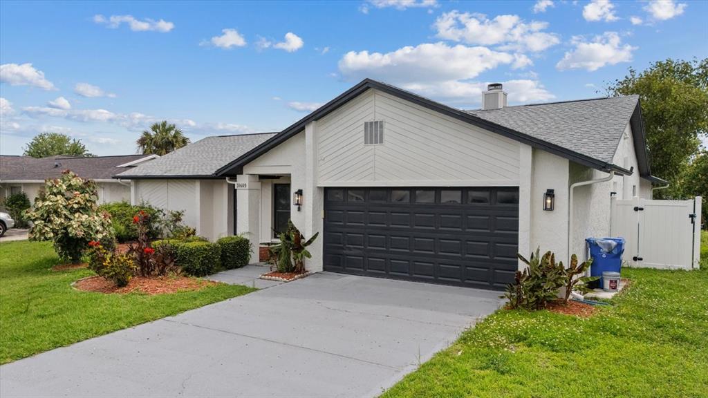 A single-story house with a white stucco exterior, a dark garage door, and a gray roof — 10609 OUT ISLAND DRIVE, TAMPA, FL