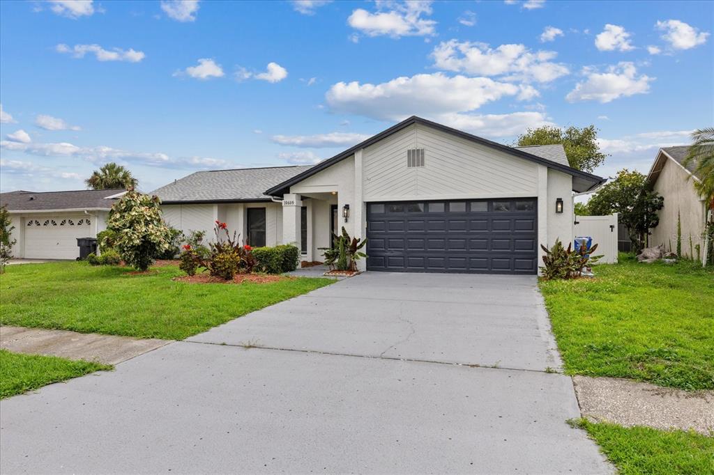 A single-story house with a white exterior, a dark garage door, and a concrete driveway — 10609 OUT ISLAND DRIVE, TAMPA, FL