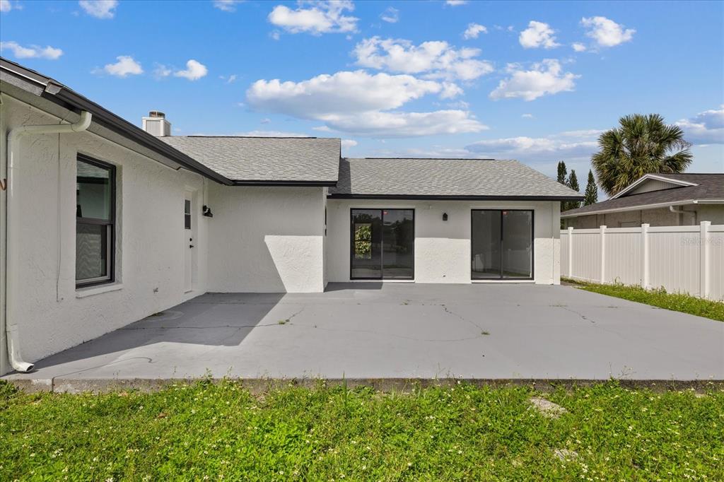 A white house exterior features a gray concrete patio and two sliding glass doors — 10609 OUT ISLAND DRIVE, TAMPA, FL