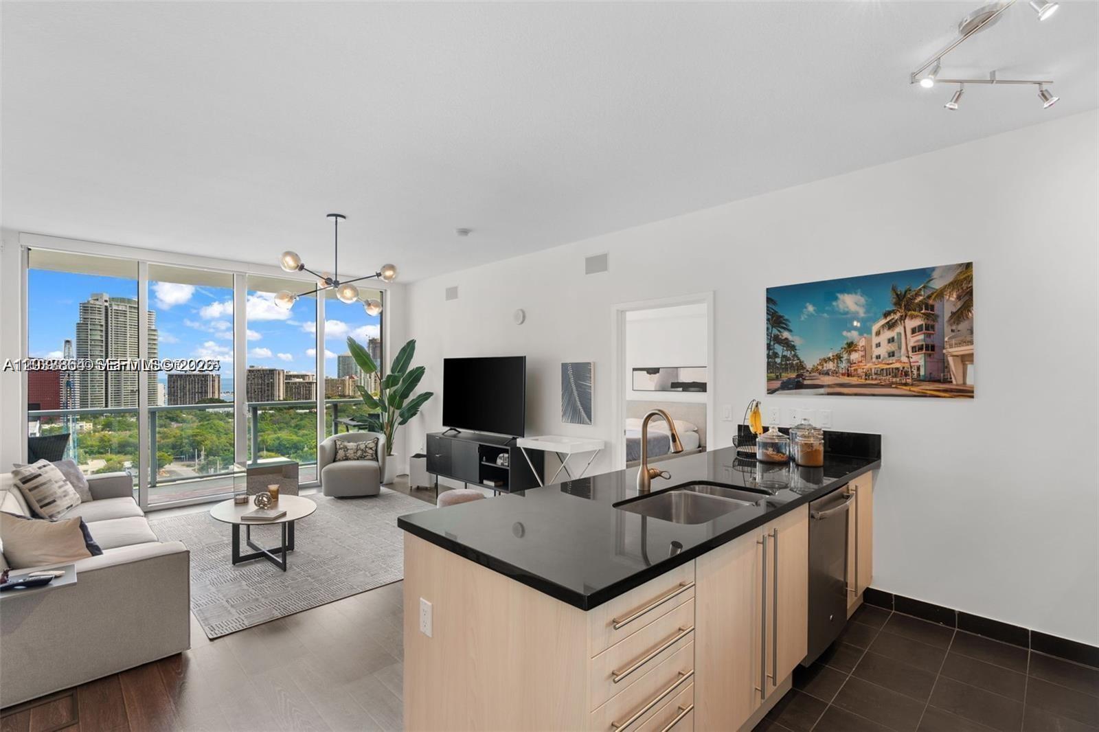 A modern apartment features an open-concept kitchen with black countertops overlooking a living area — 79 SW 12th St, Miami FL 33130, MIAMI, FL