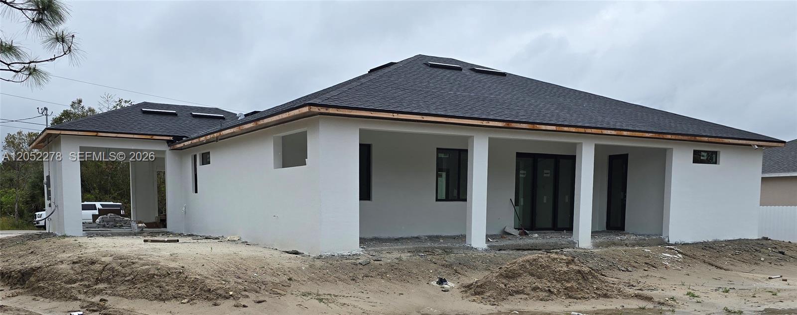 The exterior of a newly constructed white house features a dark shingled roof and patio — 728 N LaPlata Ave, Lehigh Acres FL 33974, LEHIGH ACRES, FL