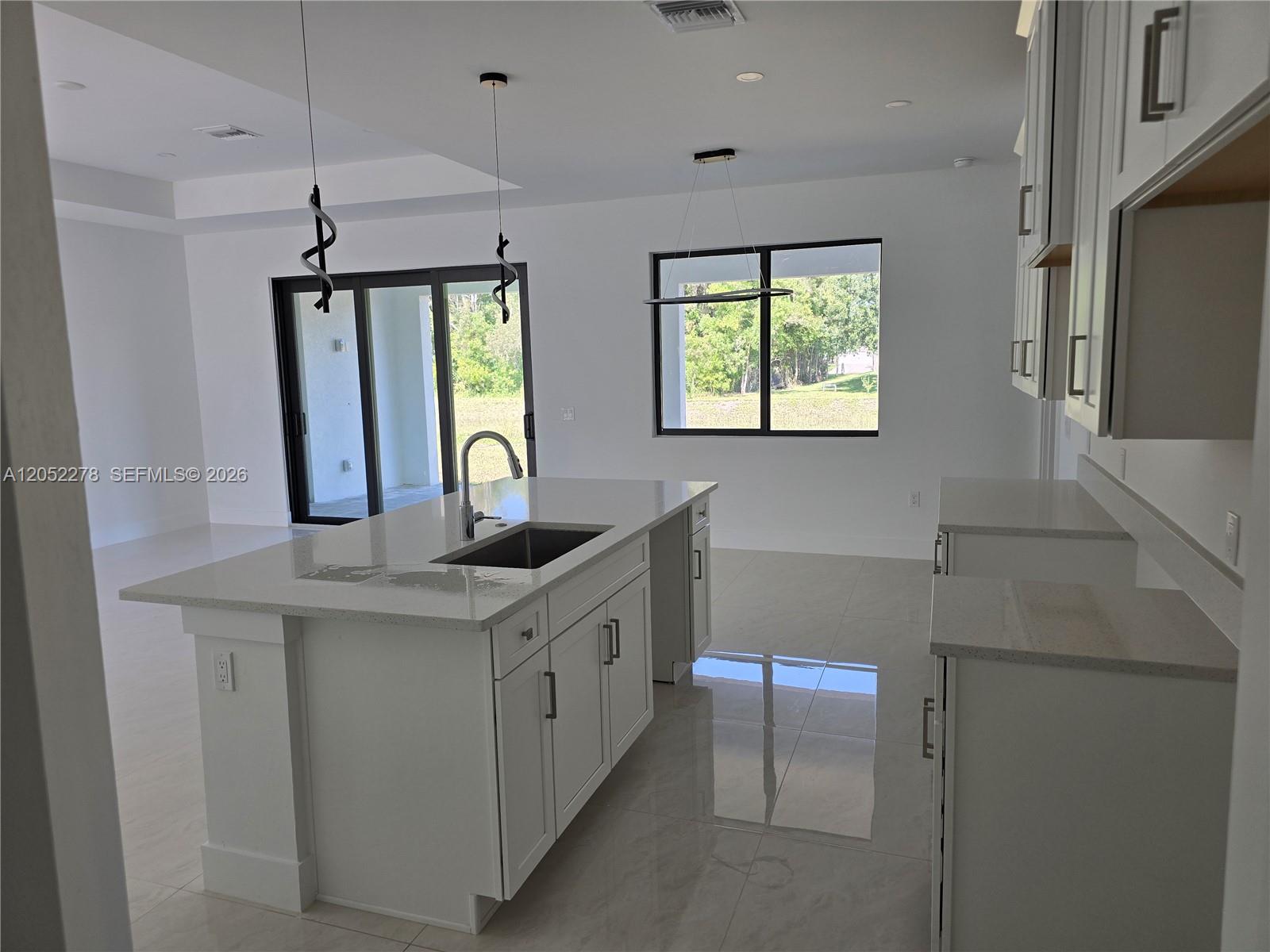 A modern kitchen features white cabinetry, a large quartz island with a sink, and tile flooring — 728 N LaPlata Ave, Lehigh Acres FL 33974, LEHIGH ACRES, FL