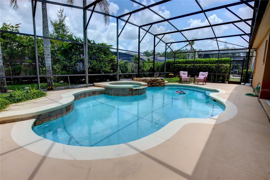 A swimming pool with an attached spa sits inside a screened-in patio enclosure — 1467 CHESSINGTON CIRCLE, LAKE MARY, FL