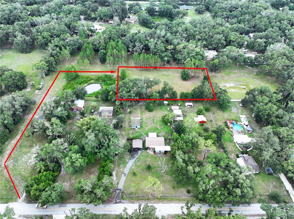 An aerial view shows a large, grassy lot outlined in red with surrounding trees and houses — 16605 HAPPY GARDEN WAY, LUTZ, FL