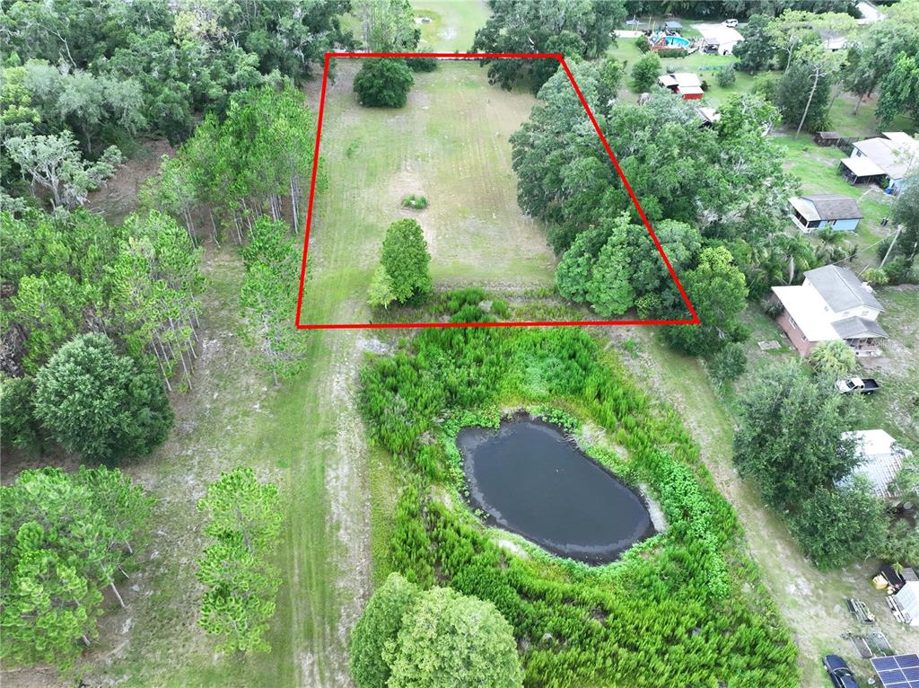An aerial view shows a rectangular plot of land outlined in red near a pond — 16605 HAPPY GARDEN WAY, LUTZ, FL
