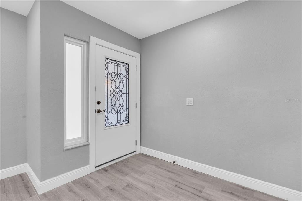 An entryway with gray walls, wood-look tile flooring, and a white door with decorative glass — 5619 DENVER STREET NE, ST PETERSBURG, FL