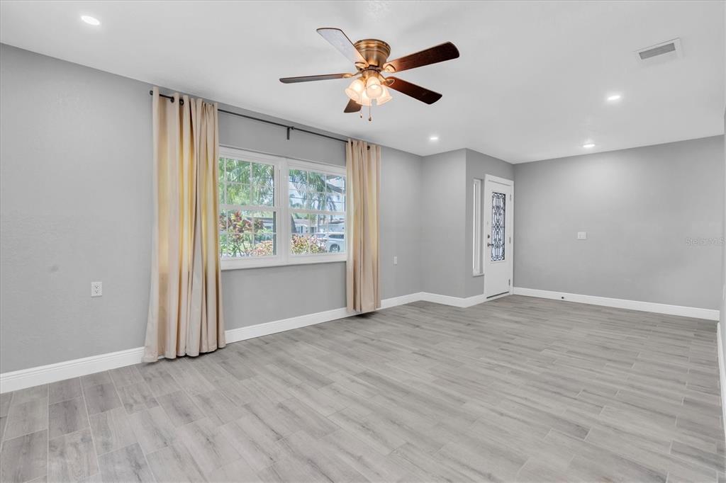 An empty living room features gray wood-look tile flooring, light gray walls, and a ceiling fan — 5619 DENVER STREET NE, ST PETERSBURG, FL
