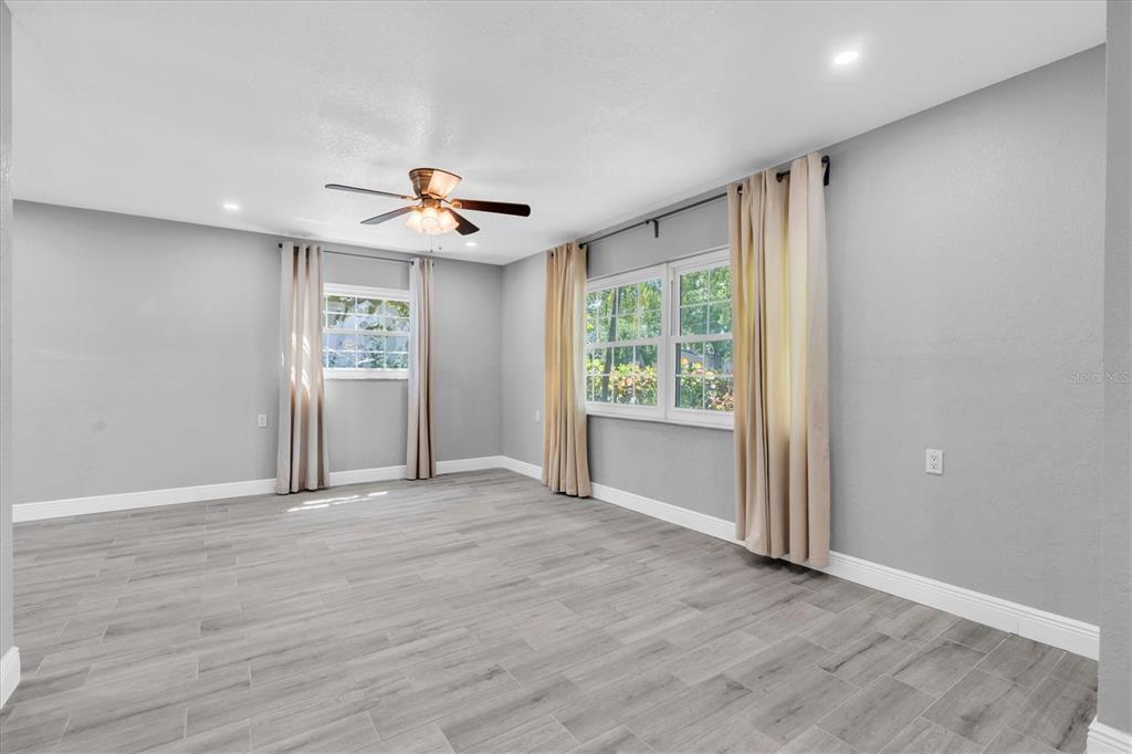 An empty room features gray walls, wood-look tile flooring, a ceiling fan, and window curtains — 5619 DENVER STREET NE, ST PETERSBURG, FL
